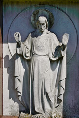 schönes Jesusfigur vor einem Grabstein mit erhobenen Händen auf einem Friedhof in Köln © Blende8