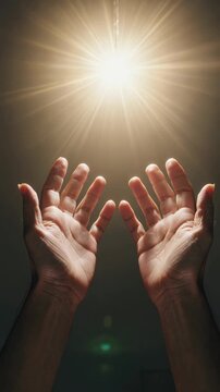 Two hands reaching up toward bright divine light from above, vertical footage