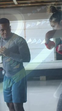 Vertical video: Coach cueing whistle boxer throwing jabs in boxing ring, red wraps, icons on wall