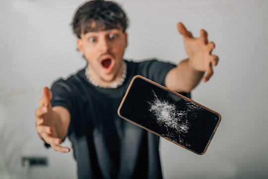 A startled young man watches as a cracked smartphone accidentally falls, reacting with panic