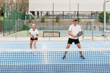 Obraz premium Senior couple enjoying an energetic game of pickleball, staying active and healthy on an outdoor sports court