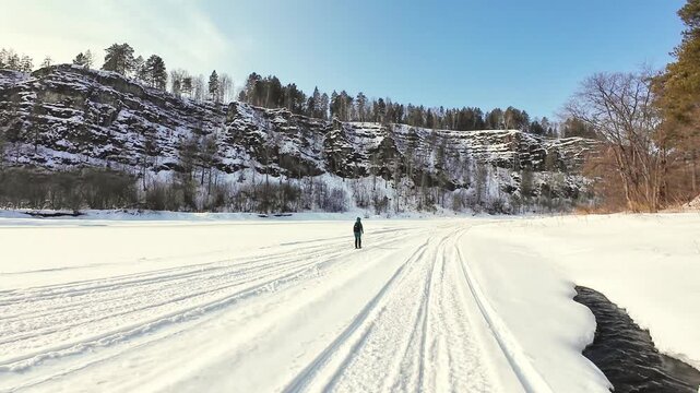Lone Skier Gliding Across Frozen Lake Under Dramatic Cliffs, Endurance Athlete Maintaining Rhythm On Parallel Tracks, Bright Sky, Snowy Ledges And Expansive Winter Expanse Evoking Challenge