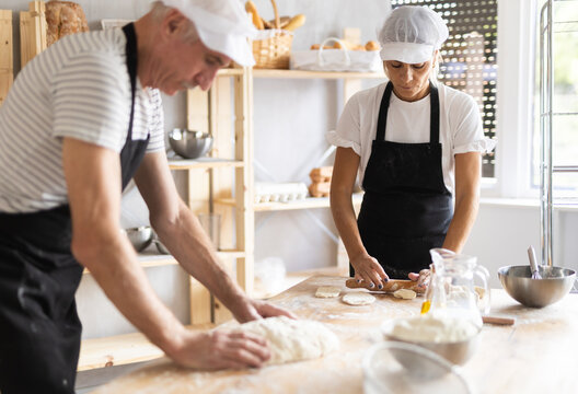Two bakers prepare dough for baking - shaping it and rolling it out with rolling pin