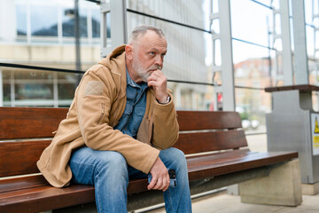 Fototapeta premium Man sits on a bench in urban area while waiting for transportation in the daytime 
