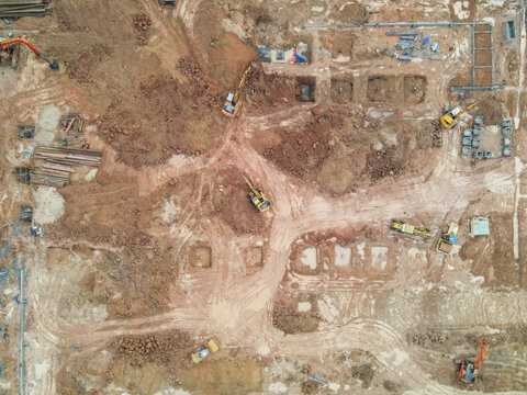 Aerial view of a large construction site with excavators digging foundation pits in reddish soil and tire tracks in An Phuoc, Dong Nai, Vietnam.