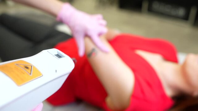 Medical specialist using a laser to remove a tattoo from a woman's arm in a beauty clinic. Modern aesthetic medicine procedure for skin cleaning and correction, erasing unwanted body art