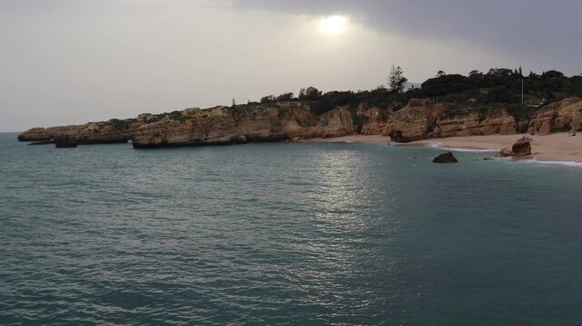Timelapse of a beach in Algarve surrounded by cliffs, featuring a dense dramatic cloud during sunset. Ocean waves and changing light create a cinematic coastal scene.