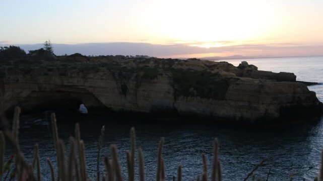 Timelapse of a beach in Algarve surrounded by cliffs, featuring a dense dramatic cloud during sunset. Ocean waves and changing light create a cinematic coastal scene.