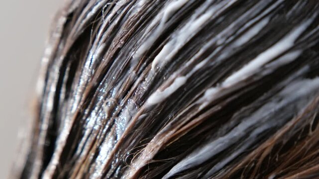 Extreme close-up macro video of wet hair strands coated with shampoo or conditioner, showing detailed texture
