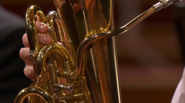 Tracking shot close up of musician hands playing tuba pressing valves on brass instrument in concert hall during live classical performance