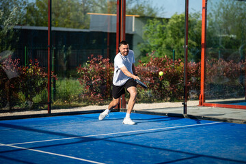 Obraz premium Man playing padel on blue court, hitting ball