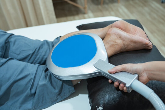 Physical therapy pms peripheral magnetic stimulation device for leg pain relief session in clinic room with patient ankle treatment and therapist hand adjustment on cushion support