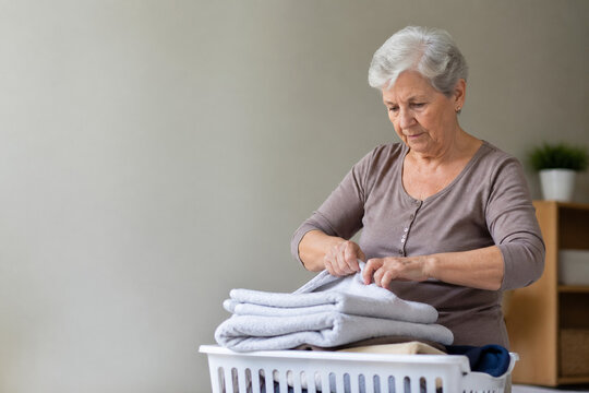 AI generated older woman folding clean laundry neatly at home in a bright living room everyday domestic routine senior lifestyle calm realistic interior