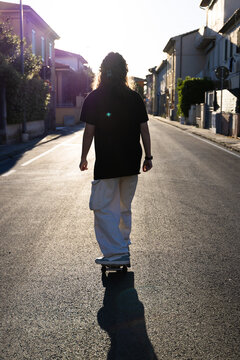 Ragazza in skate che viaggia contro sole sull'asfalto