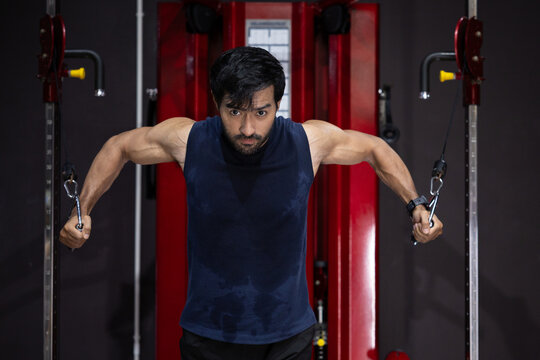 Gym fitness man cable workout strength training muscular man performing cable chest fly exercise pulley machine gym, intense focused expression, sweaty sleeveless shirt, healthy active lifestyle
