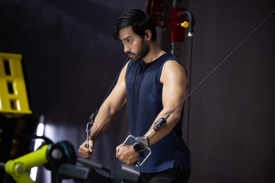Fitness man gym workout strength training cable machine athletic male doing cable chest fly exercise gym, focused expression, muscular arm, indoor fitness studio with equipment, dark background
