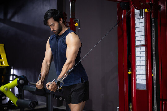 Fitness gym man workout cable machine tricep exercise strength training athlete performing cable tricep pushdown gym using pulley machine, focused expression, muscular arm, dark interior