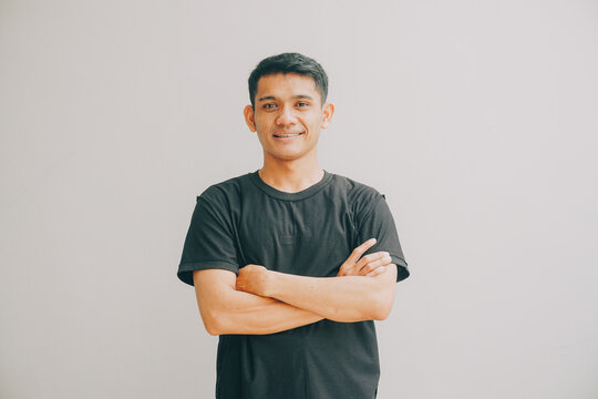 man with arms crossed smiling confidently against a plain light grey studio background
