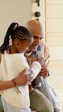 Vertical video: Arriving father with gray bag leaning, crouching at front door, greeting daughter