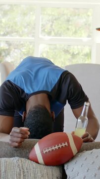 Vertical video: Leaning man blue shirt talking to camera inspecting football at home holding bottle