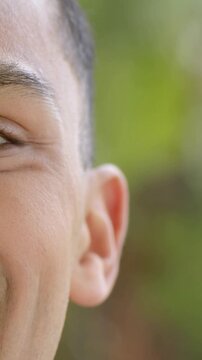 Vertical video: Smiling man showing smile deepening while eye narrowing in garden, blurred foliage