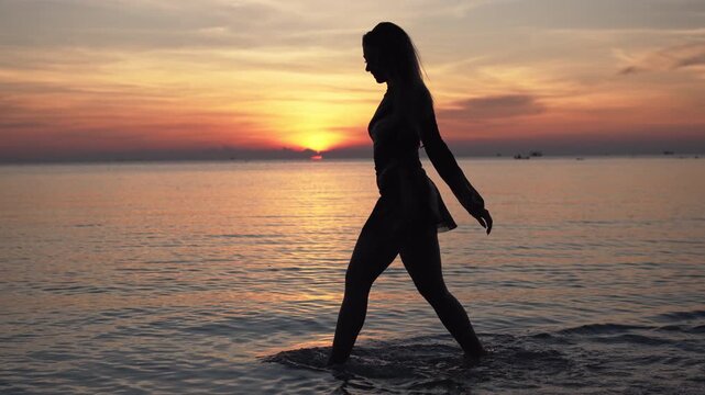4k video of a Silhouette of young female walking along beach at sunset, peaceful wellness lifestyle by the ocean