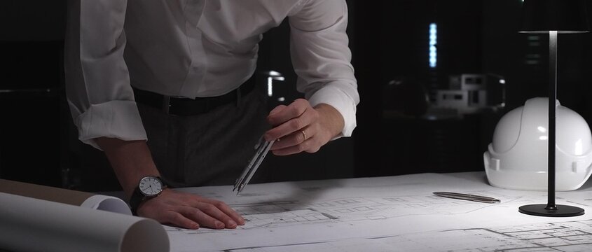 Architect designing building plans at night, working overtime on a new construction project with tools and blueprints.