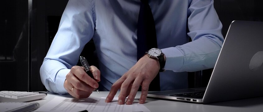 Businessman working overtime in office signing document at night, preparing contracts and finances. Audit and taxes in business