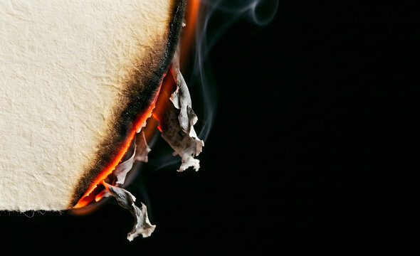 Extreme macro photography of the edge of a single sheet of textured cream paper on the far left. The edge is actively burning, showing a glowing bright orange ember line consuming the paper.