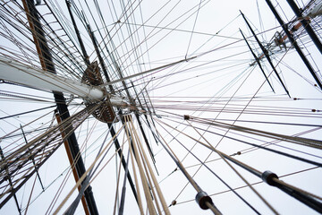 Ropes and lines stretch across the view of a sailing ship. The mast stands tall as the ship is prepared for the open sea. The sky is overcast and emphasizes the rigging. © Videophilia