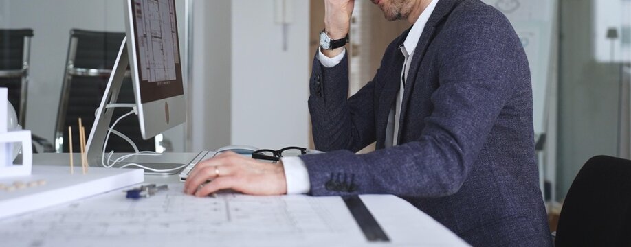 Frustrated man suffering from stress and exhaustion at work, holding his head, feeling overwhelmed by professional pressure. Business and architecture concept
