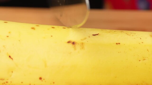 Close-up of a sharp knife blade cutting a ripe yellow banana in half, highlighting the skin details.