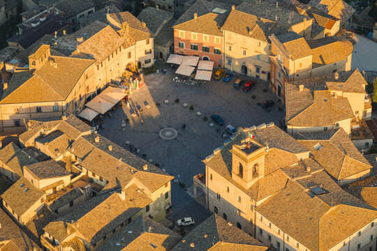 Aerial view of the historic Piazza del Comune surrounded by stone buildings and terracotta rooftops during golden hour in Montefalco, Umbria, Italy.