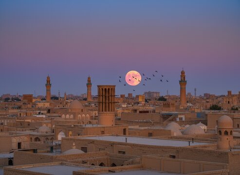 Full moon over yazd cityscape with windcatcher and minarets at dusk
