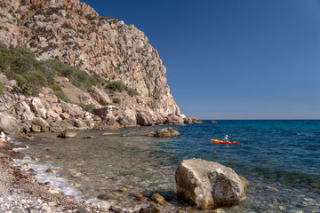 Naklejka premium Kayak coastline sea person paddling orange kayak along a beautiful rocky coastline peaceful summer adventure clear turquoise water