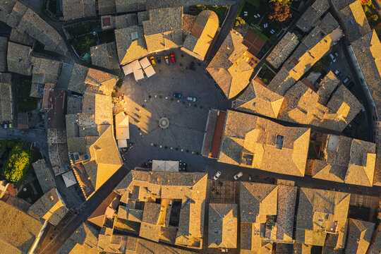 Aerial view of the historic circular town square surrounded by ancient stone buildings and tiled rooftops during golden hour in Montefalco, Umbria, Italy.