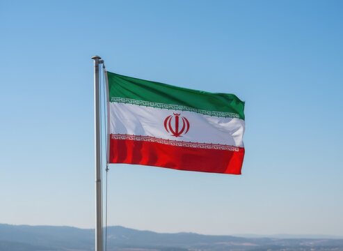 The national flag of iran waving on a metal pole against a clear blue sky