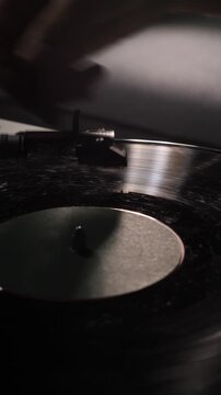 Vertical video turntable stylus playing a black vinyl record in motion, creating an immersive analog listening experience within a dark and ambient setting