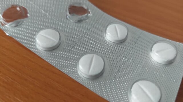 Partially empty blister pack of white pharmaceutical pills on wooden surface