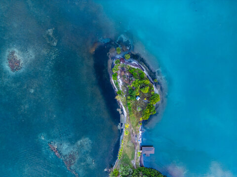 Aerial view of the lush tropical island of Guanaja with vibrant green vegetation and a small wooden dock surrounded by turquoise Caribbean waters Guanaja, Bay Islands Department, Honduras.