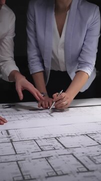 Architects and engineers collaborating on a building blueprint, measuring and discussing plans for a new construction project. Concept of architecture and business in low key lighting