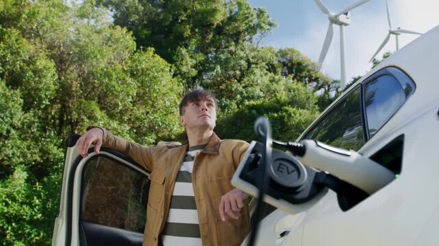 Proud Man Charging Electric Vehicle Near Wind Turbines for a Sustainable Net Zero Future