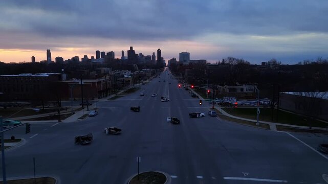 Aerial tracking shot of city skyline and traffic moving along wide avenue at dusk