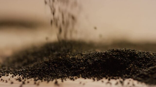 Slow motion handheld close up of dark granules pouring and accumulating on wooden tabletop in studio with shallow depth of field