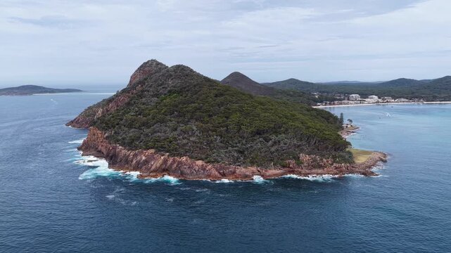 Aerial drone video panning around Tomaree Mountain in Port Stephens, New South Wales, Australia. Scenic coastal landscape showing prominent headland, rugged terrain and surrounding ocean environment.