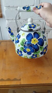 Person holding enamel painted kettle with flowers, showing from different angles, vertical, first person view