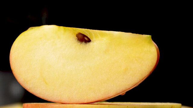 Stunning macro shot of a juicy, golden apple slice standing out against a mysterious black background.