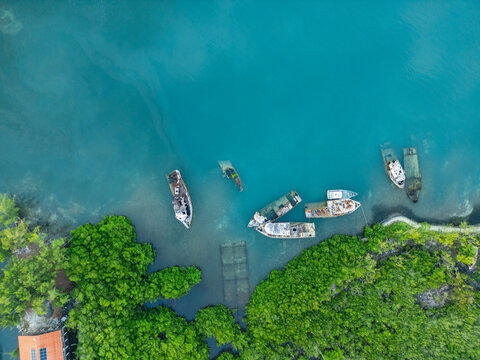 Aerial view of several shipwrecks and abandoned boats resting in turquoise water along a lush green shoreline in Guanaja, Bay Islands Department, Honduras.
