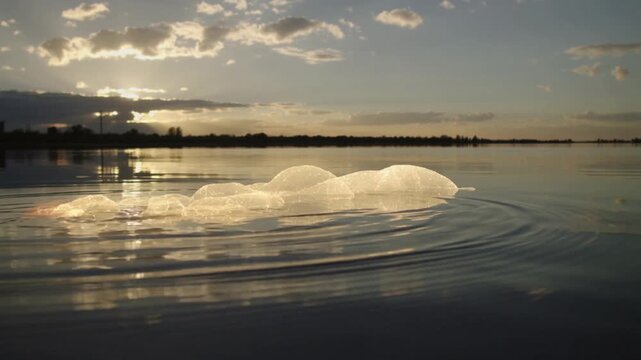 Iceberg floating on calm lake water with ripples at sunset