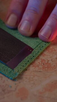 Vertical 4K ASMR video of a craftsman skiving the edge of green leather with a sharp Japanese knife.